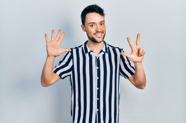 Gündelik kıyafetler giyen genç İspanyol adam sekiz numarayı gösterip işaret ederken kendinden emin ve mutlu bir şekilde gülümsüyor.. 