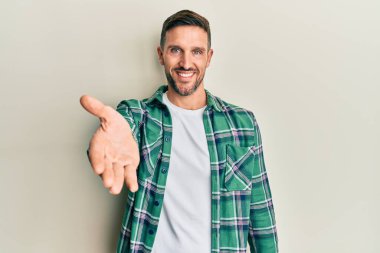 Yakışıklı, sakallı, sıradan kıyafetler giyen, gülümseyerek dostça tokalaşan ve hoş geldin diyen bir adam. başarılı iş. 