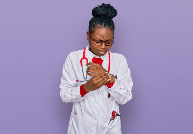 Genç Afro-Amerikan kadın doktor üniforması giyiyor ve steteskop takıyor. Ellerinde ve parmaklarında ağrı var, eklem iltihabı var. 