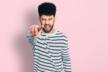 Sakallı, sıradan çizgili süveter giyen genç Arap adam kameraya kızgın ve sinirli bir şekilde bakıyor. 