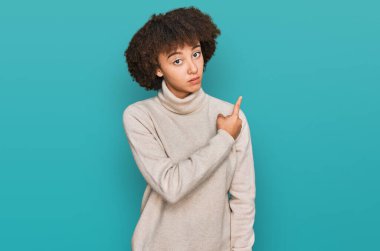 Kışlık yün kazak giyen genç İspanyol kız elini kaldırmış reklamını yapıyor, ciddi ve sakin bir yüz ifadesi var. 