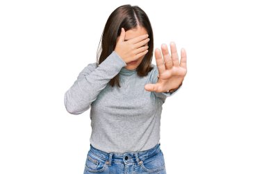 Balıkçı yaka kazak giyen genç ve güzel bir kadın elleriyle gözlerini kapatıyor ve üzgün ve korku ifadeleriyle jest yapıyor. utangaç ve olumsuz kavram. 