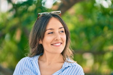 Genç İspanyol kadın gülümsüyor. Parkta güneş gözlüğüne dokunduğu için mutlu..