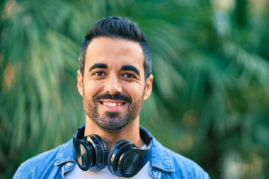 Şehirde kulaklık takarak mutlu gülümseyen genç İspanyol adam..