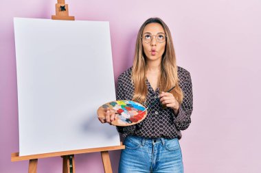 Güzel İspanyol kadın paletle resim çiziyor, resim sehpası ayakta duruyor, ağzı balık gibi bakıyor, gözlerini kıstırıyor, çılgın ve komik.. 