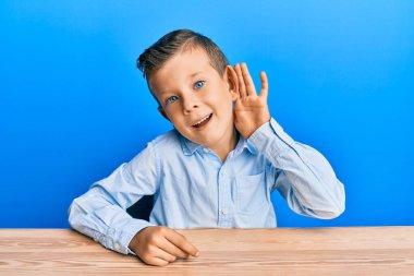 Kafkasyalı sevimli çocuk, gündelik giysiler içinde masada oturmuş, sırıtarak dedikodu ya da dedikoduları dinliyor. Sağırlık kavramı. 