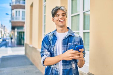 Genç İspanyol adam şehirde akıllı telefon kullanarak mutlu gülümsüyor..