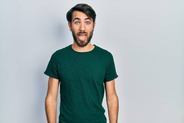 Günlük beyaz tişört giyen genç İspanyol adam komik bir ifadeyle dilini dışarı çıkarıyor. duygu kavramı. 