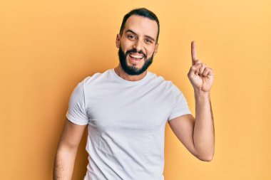 Gündelik beyaz tişört giyen sakallı genç adam başarılı bir fikri işaret ediyor. Heyecanlı ve mutlu. Bir numara.. 
