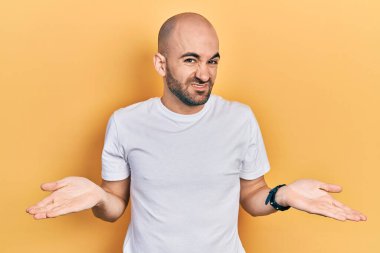 Gündelik beyaz tişört giyen genç kel bir adam habersiz ve kolları açık, hiçbir fikri yok.. 