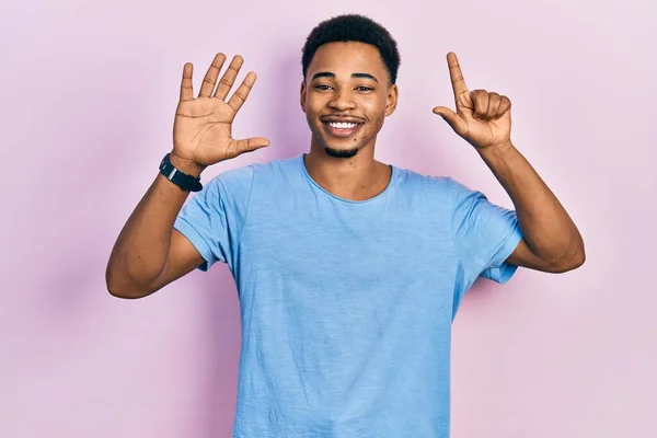 自信を持って幸せな笑顔ながら 若いアフリカ系アメリカ人の男は カジュアルな青のTシャツを着て指の数7を示すと指摘 — ストック写真