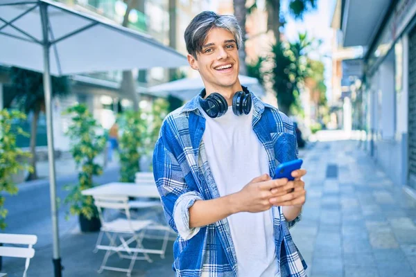 若いヒスパニック系の男は 市内でスマートフォンやヘッドフォンを使用して幸せな笑顔 — ストック写真