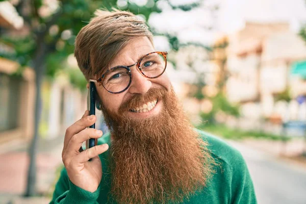 若いですアイルランドの男で赤毛の髭は笑顔で幸せと街のスマートフォンで話して — ストック写真