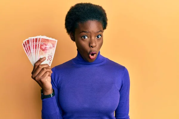 Chica Afroamericana Joven Sosteniendo Billetes Shekels Israelíes Asustada Sorprendida Con —  Fotos de Stock