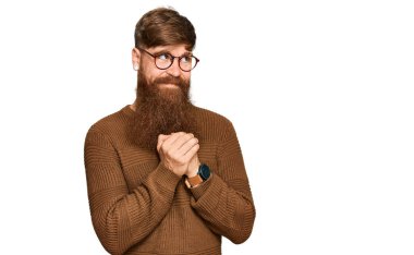 Genç İrlandalı kızıl elbiseli ve gözlüklü adam. Gergin ve heyecanlı bir şekilde gülümsüyor. Elleri çenesinde yan tarafa bakıyor. 