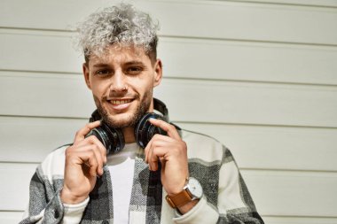 Şehirde kulaklık takarak mutlu gülümseyen genç İspanyol adam..