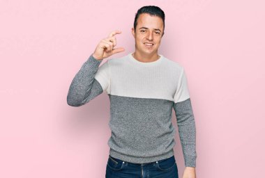 Kış süveteri giyen yakışıklı genç adam gülümsüyor ve kendine güvenen el hareketleriyle küçük boy işareti yapıyor parmakları bakıyor ve kameraya bakıyor. ölçüm kavramı. 