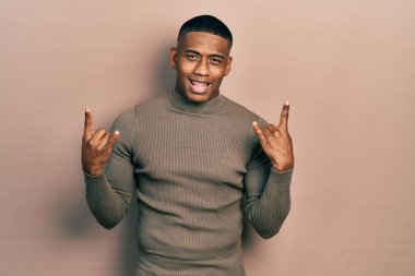 Balıkçı yaka kazak giyen genç bir zenci çılgın bir ifadeyle bağırıyor elleri havada rock sembolü yapıyor. Müzik yıldızı. ağır kavram. 