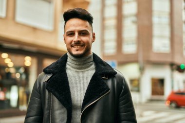 Genç Arap adam gülümsüyor, mutlu bir şekilde şehirde duruyor..