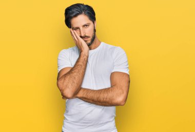 Günlük beyaz tişört giyen genç İspanyol adam kollarını kavuşturup depresyondan sıkılmış ve yorgun görünüyor.. 