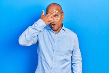 Orta yaşlı, sıradan kıyafetler giyen ve gözlüklü bir adam. Şoka girmiş, yüzünü ve gözlerini kapamış, utanmış bir ifadeyle parmaklarından bakıyor.. 