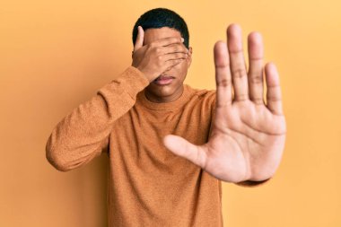 Genç, yakışıklı, günlük kazak giyen, elleriyle gözlerini kapatan üzgün ve korku ifadeleriyle jestler yapan İspanyol bir adam. utangaç ve olumsuz kavram. 