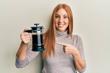 Fransız kahve makinesini tutan genç İrlandalı kadın mutlu bir şekilde el ve parmak işareti yapıyor. 
