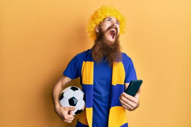 Kızıl saçlı, uzun sakallı futbol holiganları tezahürat yapıyor. Akıllı telefonu elinde tutuyor. Kızgın ve öfkeli çığlıklar atıyor.. 