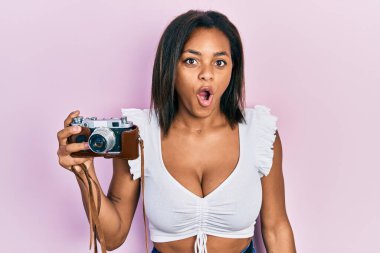 Genç Afrikalı Amerikalı kız elinde antika bir kamera tutuyor. Korkmuş ve ağzı açık kalmış, şaşırmış ve şaşırmış. İnanmayan yüz. 