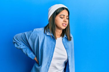 Sırt ağrısından muzdarip sevimli yün şapkalı genç Latin kadın, elleriyle dokunuyor, kas ağrısı çekiyor. 