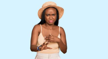 Yazlık şapkalı genç siyahi kadın tiksindirici bir ifade takınıyor, tiksindirici bir ifade takınıyor ve tiksindirici bir ifade takınıyor. Eller havada. 