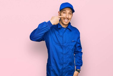 Sakallı, inşaatçı tulumu giymiş, kel bir adam. Parmakla yüzünü ve burnunu gösteriyor. Neşeli gülümsüyor. güzellik konsepti 