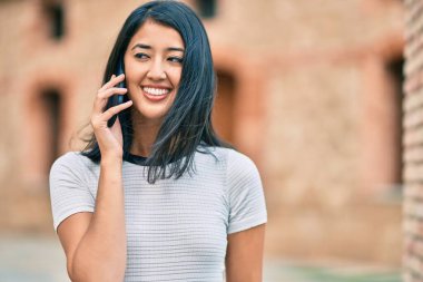 Genç İspanyol kadın gülümsüyor. Şehirdeki akıllı telefondan konuşuyor..