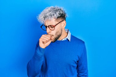 Modern boyalı saçlı, süveter ve gözlük takan, kendini kötü hisseden ve soğuk algınlığı veya bronşitin belirtisi olarak öksüren İspanyol genç bir adam. sağlık hizmeti kavramı. 