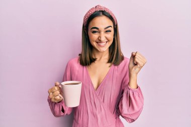 Genç esmer kız bir fincan kahve içiyor gururla bağırıyor, zaferi kutluyor ve başarıyı kollarını kaldırarak kutluyor. 