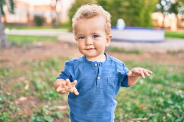 Sevimli ve mutlu küçük çocuk güneşli bir günde parkta eğleniyor. Güzel sarı saçlı erkek çocuk dışarıda oynuyor.