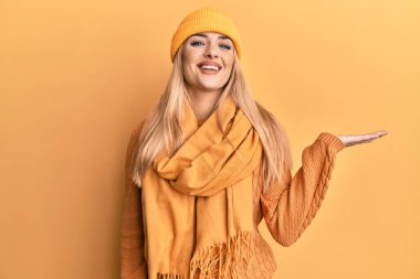 Beyaz kadın yün kazak ve kep giymiş neşeli bir şekilde gülümsüyor ve avuç içi kameraya bakıyor.. 