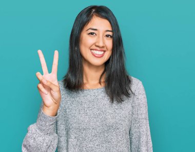 Güzel Asyalı genç kadın gündelik giysiler giyip iki numarayı gösterip işaret ederken kendinden emin ve mutlu gülümsüyor.. 