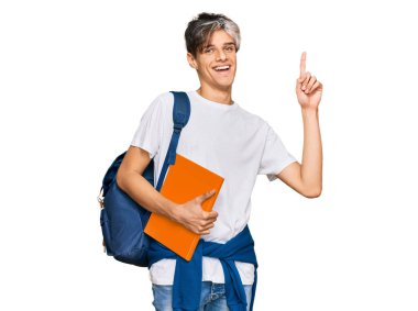 Sırt çantası takan ve elinde kitaplarla gezen İspanyol asıllı genç bir adam bir fikir veya soruyla şaşırmış ve mutlu bir yüzle işaret ediyor. 