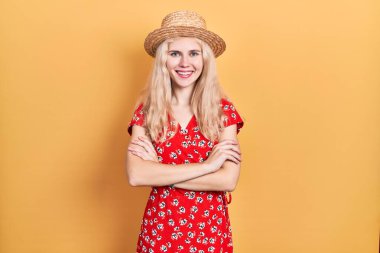 Sarı saçlı, yaz şapkası takan, kollarını kavuşturup kameraya gülümseyen güzel beyaz kadın. pozitif kişi. 