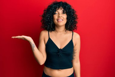 Kolsuz tişörtlü, sıradan giyinen, neşeli gülümseyen, avuç içi kameraya bakan genç İspanyol kadın.. 