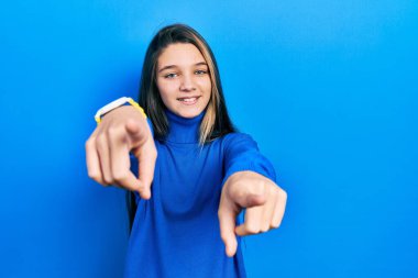 Balıkçı yaka kazak giyen genç esmer kız parmaklarıyla seni ve kamerayı işaret ediyor. 