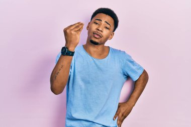 Genç, Afro-Amerikan bir adam, günlük mavi tişörtler giyiyor, İtalyan jestleri yapıyor, elleri ve parmakları kendinden emin. 