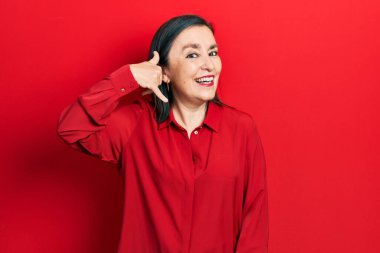 Orta yaşlı İspanyol kadın, günlük kıyafetler giyip gülümsüyor telefonla el ve parmak hareketleri yapıyor telefonda konuşuyor gibi. iletişim kavramları. 