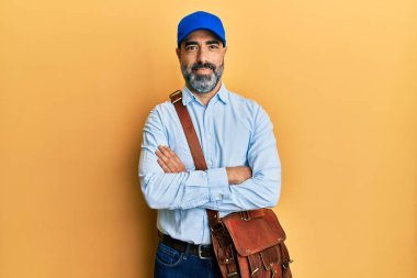 Orta yaşlı, sakallı, gri saçlı, kurye şapkalı mutlu yüzlü, kollarını kavuşturup kameraya bakan bir adam. pozitif kişi. 