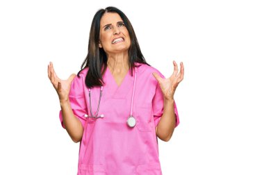 Orta yaşlı esmer kadın doktor üniforması giyiyor ve steteskop deli deli bağırıyor ve bağırıyor agresif bir ifade ve kollar havada. hüsran kavramı. 