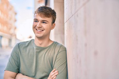 Kollarını kavuşturmuş genç beyaz adam şehirde mutlu bir şekilde gülümsüyor..