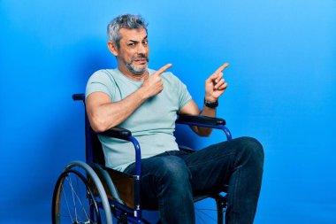 Yakışıklı, orta yaşlı, gri saçlı, tekerlekli sandalyede oturan, endişeli ve gergin, endişeli ve şaşırmış bir adam. 