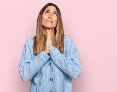 Gündelik kıyafetler giyen genç bir kadın elleri bağlı yalvarıyor ve dua ediyor. Yüzünde umut ifadesi var. Duygusal ve endişeli. Yalvarıyor. 