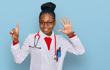 Genç Afro-Amerikan kadın doktor üniforması ve steteskop giyiyor. Altıncı parmaklarını gösterip gösterirken kendinden emin ve mutlu gülümsüyor.. 